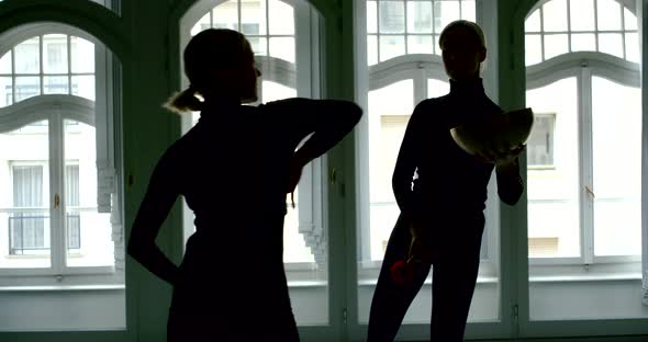 A Slender Blonde Girl Is in a Large Studio with Large Windows, She Is Holding a Bowl and a Stick