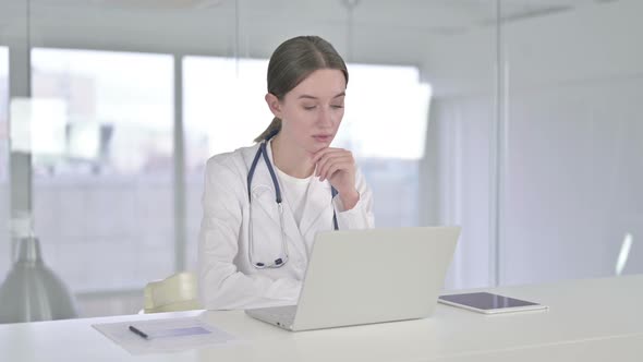 Young Female Doctor Thinking and Working on Laptop in Office