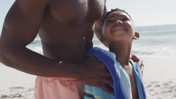 Smiling african american father toweling off his son on sunny beach