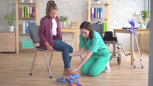 Doctor Helps in Rehabilitation To Stretch the Leg with the Help of a Roller of a Teenage Girl in a