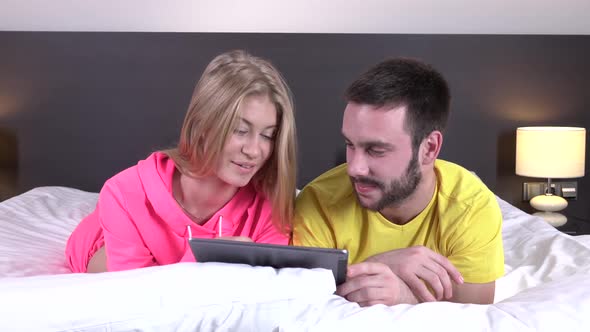 Smiling Relaxed Young Couple Using Digital Tablet in Bed at Home