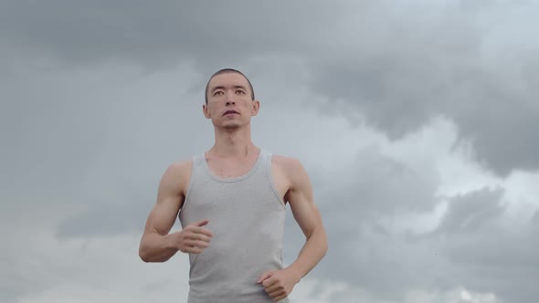 Man of Asian Appearance Runs with Concentration Against Background of Thunderstorms Sky Front View