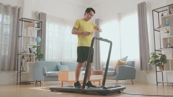 Asian Man Looking Smart Watch And Training On Walking Or Running Treadmill At Home
