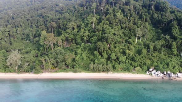 A drone video flying outward from an empty Tioman tropical island with full of trees and tropical fo