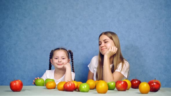 Girls sitting at table with fruits. Smiling girl with fresh fruit on table isolated over blue backgr