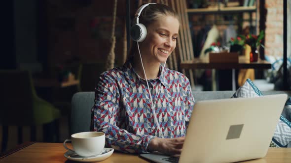 Happy Lady Enjoying Music in Headphones Singing Dancing Using Laptop in Cafe