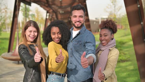 Four young friends show their thumbs to the camera. Beautiful multi-ethnic group