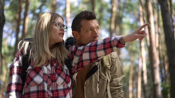 Curios Young Woman Pointing Looking Away Showing Man Destination in Sunny Forest