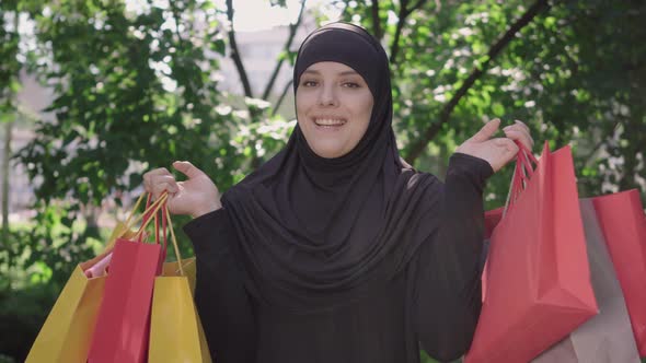 Cheerful Young Muslim Woman Raising Hands with Shopping Bags and Smiling at Camera. Portrait of