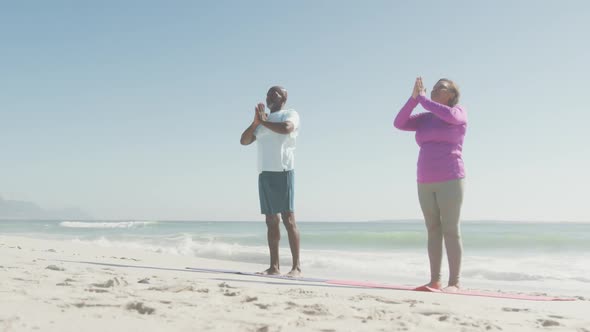 Senior african american couple practicing yoga on mats on sunny beach