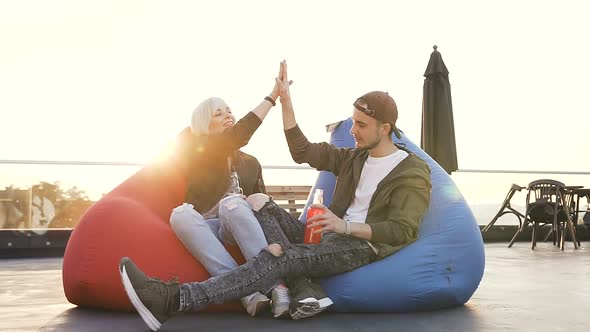 Young Guy and Girl are Sitting in Multi-colored Armchairs in Terrace Cafe