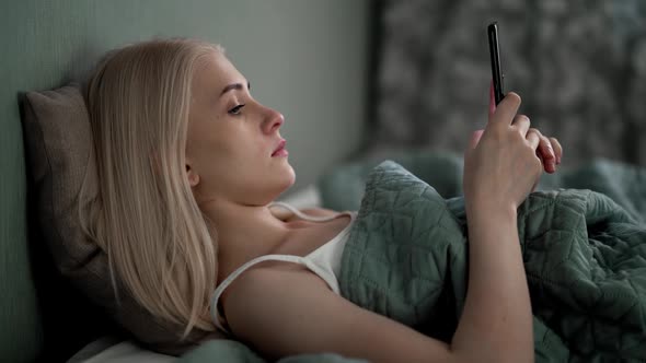 The Girl Lies in Her Bed and Looks at the News on Social Networks