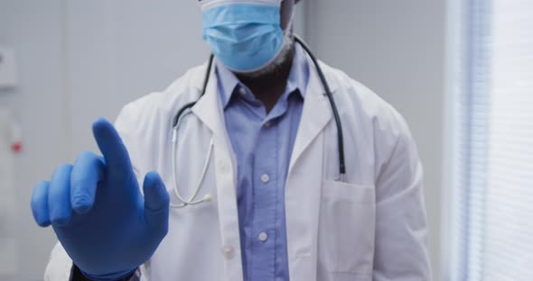 Midsection of african american male doctor wearing face mask and surgical gloves
