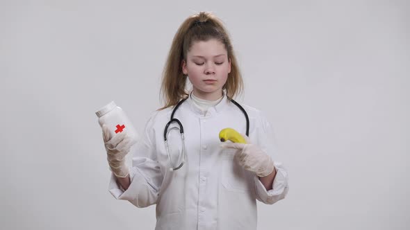 Caucasian Little Doctor Choosing Between Pills and Banana Stretching Fruit to Camera Shaking Head