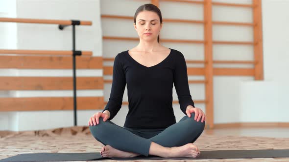 Attractive Young Woman Exercising and Sitting in Yoga Lotus Position While Resting in Studio