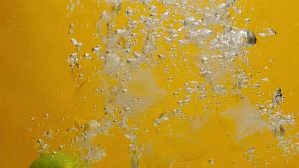 Closeup of Falling Limes and Ice Into the Water on Orange Background Making a Cocktail of Citrus