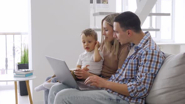 Happy Young Couple with Kid Sitting on Couch at Home Laptop Having Video Call