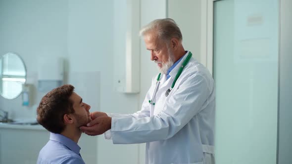 Side View of Mature Physician Otolaryngologist Touching Lymph Nodes on Neck and Examining Throat of