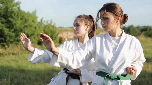 Two Young Girls in White Kimonos Demonstrate Karate Techniques in Outdoor Training. Close-up. Slow