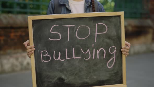 Little Girl Standing Demonstrating Alone Holding and Raising Schoolboard with Text Stop Bullying on