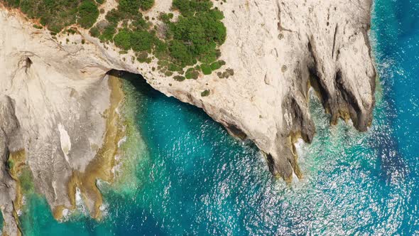 Top view of rocky coastline with cave and turquoise sea water.