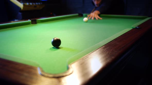 A man potting the eight ball. The black 8-ball pots in to the corner pocket to win the game