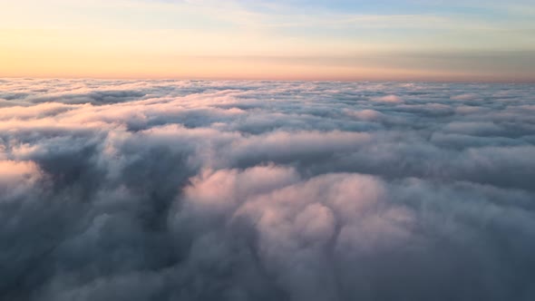 Aerial view of bright yellow sunset over white dense clouds with blue sky overhead.