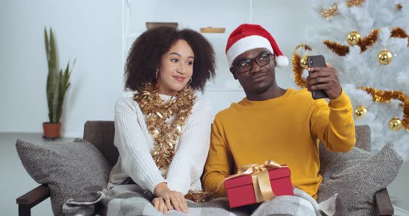 Happy Young African American Couple Recording Video Message Sitting on Sofa Near Christmas Tree