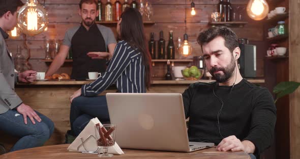 Young Bearded Man Looking at His Laptop Screen While Working Remotely From a Coffe Shop