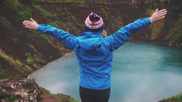 Young Tourist Woman in Jacket and Hat Rise Her Hands Enjoying Beautiful View of Kerid Lake of