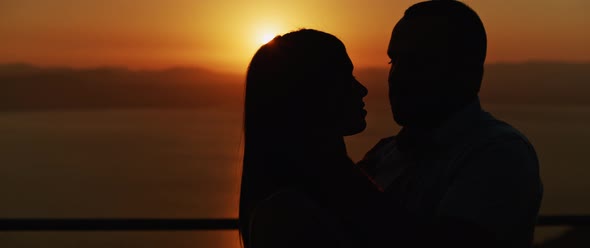 Close up of a young couple embracing at sunset, spending a romantic evening together. Slow motion.  