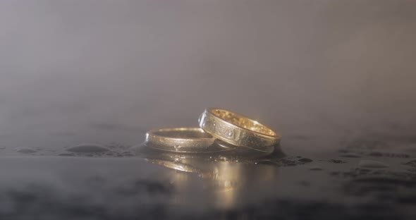 Wedding Rings on Dark Water Surface Shining with Light. Close Up Macro