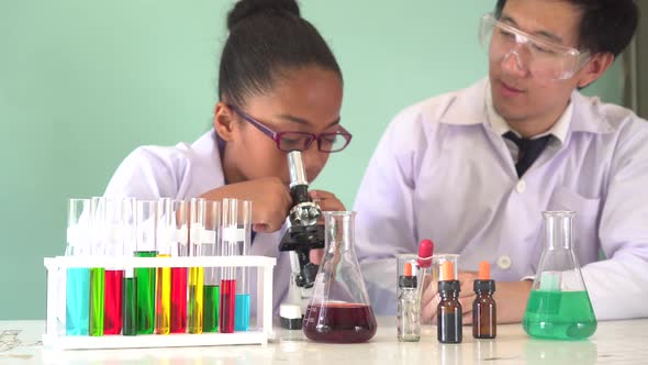 Asian Scientist Teaching African American Kid How to Use Microscope in Science Classroom