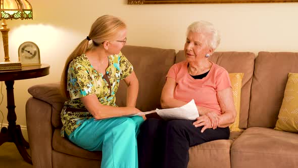Front view of home healthcare nurse and elderly woman sitting on a couch looking over paperwork.