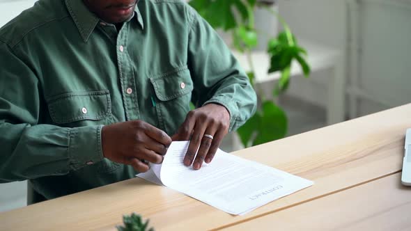 Young Businessman Reads and Signs Contract at Table in Modern Office Spbas