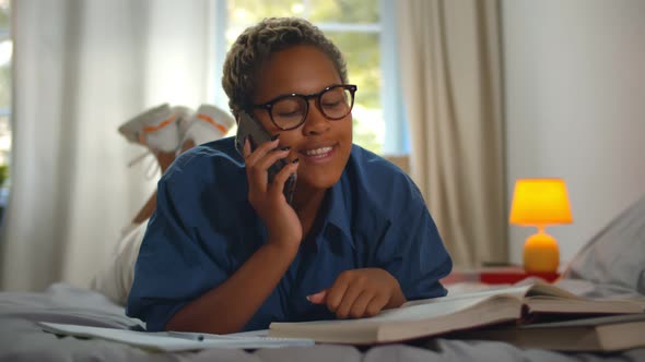 Female College Student Lying On Bed Talking on Mobile Phone And Studying