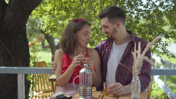 Young Happy Couple Sitting Outdoors at the Small Table Talking and Drinking Tea