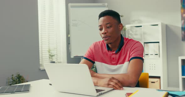 Trainee in Office Sits at Desk in Front of Laptop Monitor in Background Whiteboard Young Darkskinned