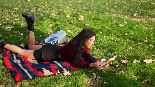 A beautiful adult woman student reading a book and relaxing in the park before her college literatur