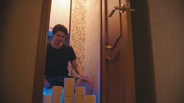 A Young Man Sitting on a Toilet with a Bunch of Toilet Paper and Closes the Door