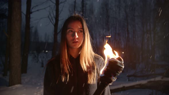 Young Woman with Torch Standing in Winter Forest Under the Snowfall