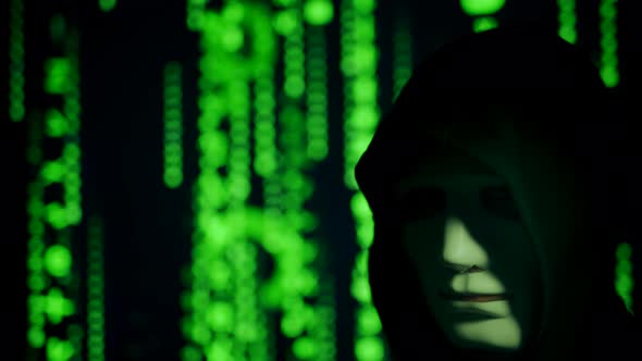 Close Up of a Anonymous Computer Hacker in Black Hood and Mask Over Abstract Binary Matrix