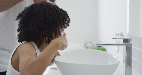 Happy biracial man and his son washing teeth in bathroom