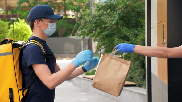 Delivery Man Wears Protective Medical Face Mask and Gloves Picks Up Paper Bag