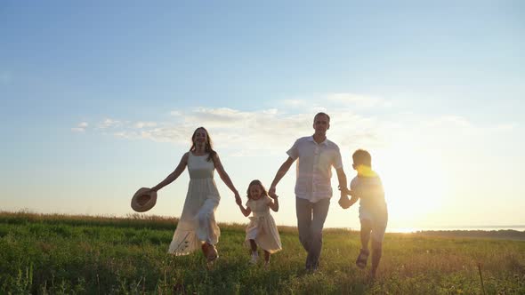 Happy Family Runs on Green Lawn at Back Sunset on Blue Sky