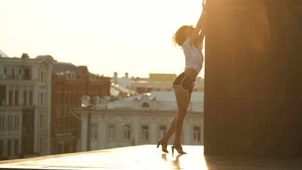 A Young Attractive Woman with Curly Hair Performing Dancing Elements Leaning on the Tower -