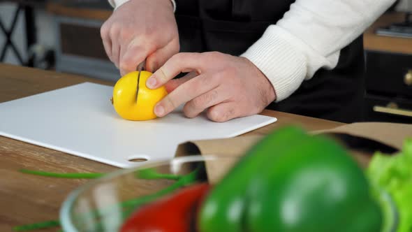Hands chef man in apron standing near table cuts lemon on board in home kitchen