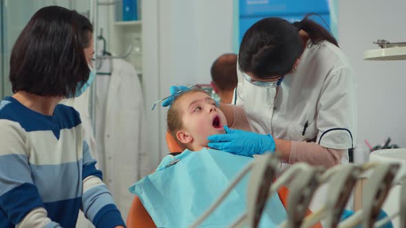 Pediatric Dentist with Mask Treating Teeth To Little Girl Patient