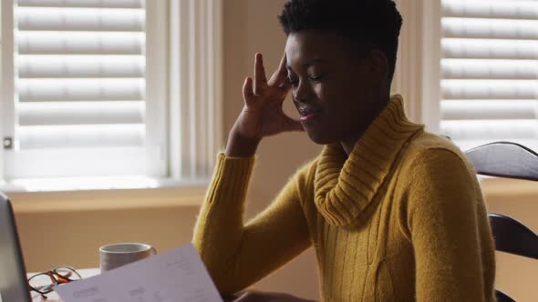 Stressed african american woman holding a document while working from home