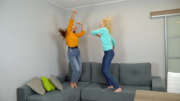 women with light and dark hair jump together on large sofa in the living room.